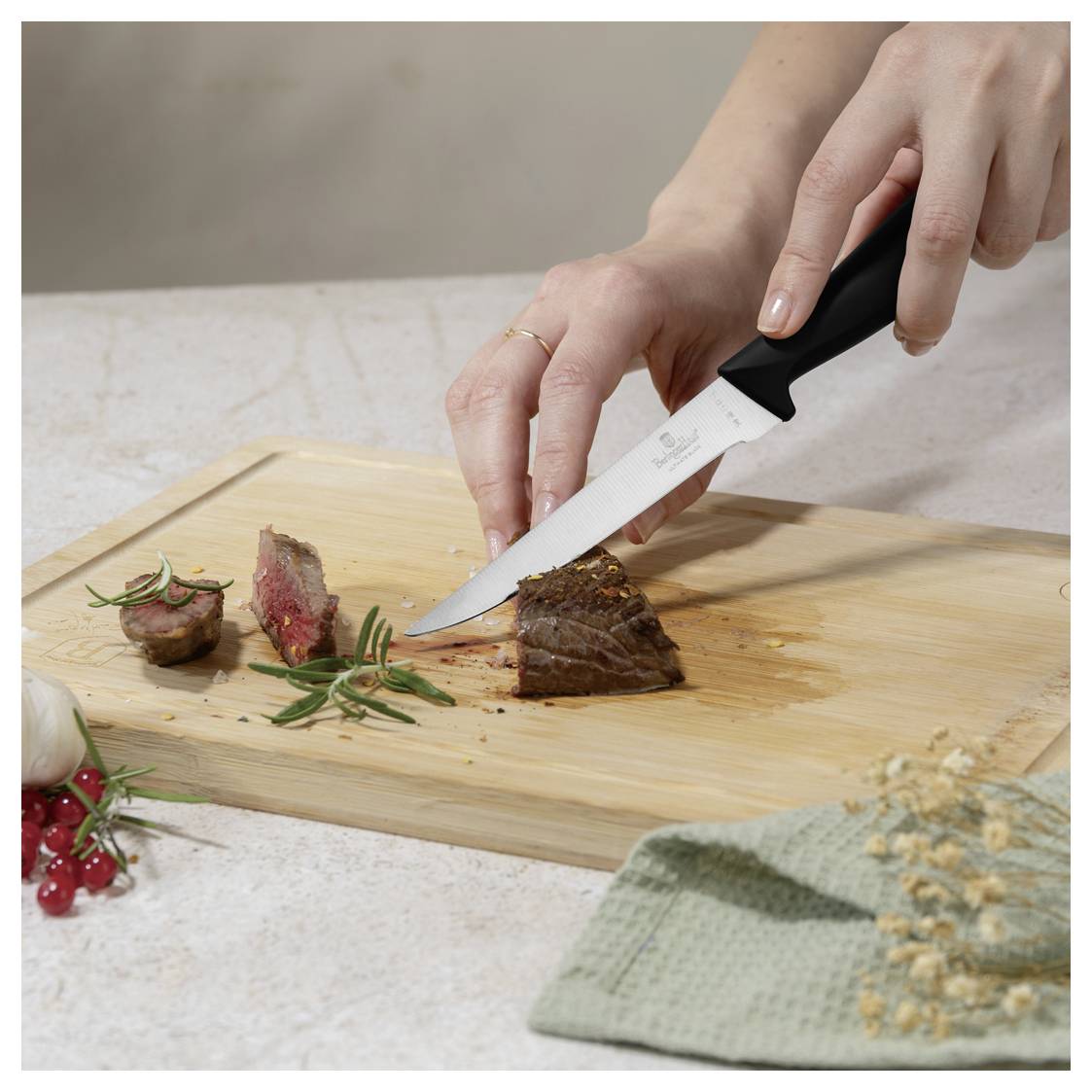 Ruky krájajú varené steak na drevenom krájacom prkne s chefským nožom, v blízkosti sú bylinky a plátovaná garnizácia.
