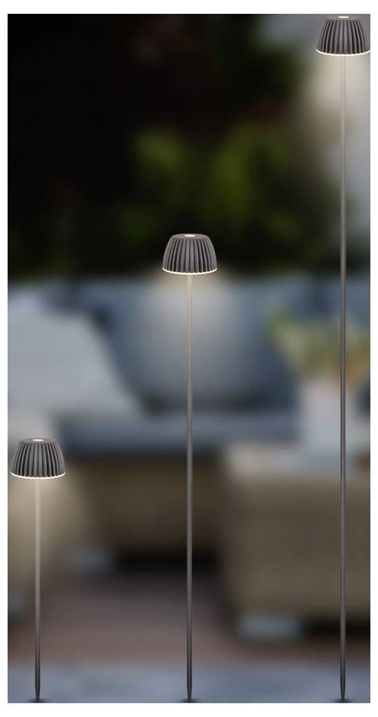 Tri štíhle moderné stojace lampy s postupne sa zvyšujúcimi výškami svietia v rozmazanom interiérovom prostredí obývacej izby a vytvárajú atmosférické osvetlenie.