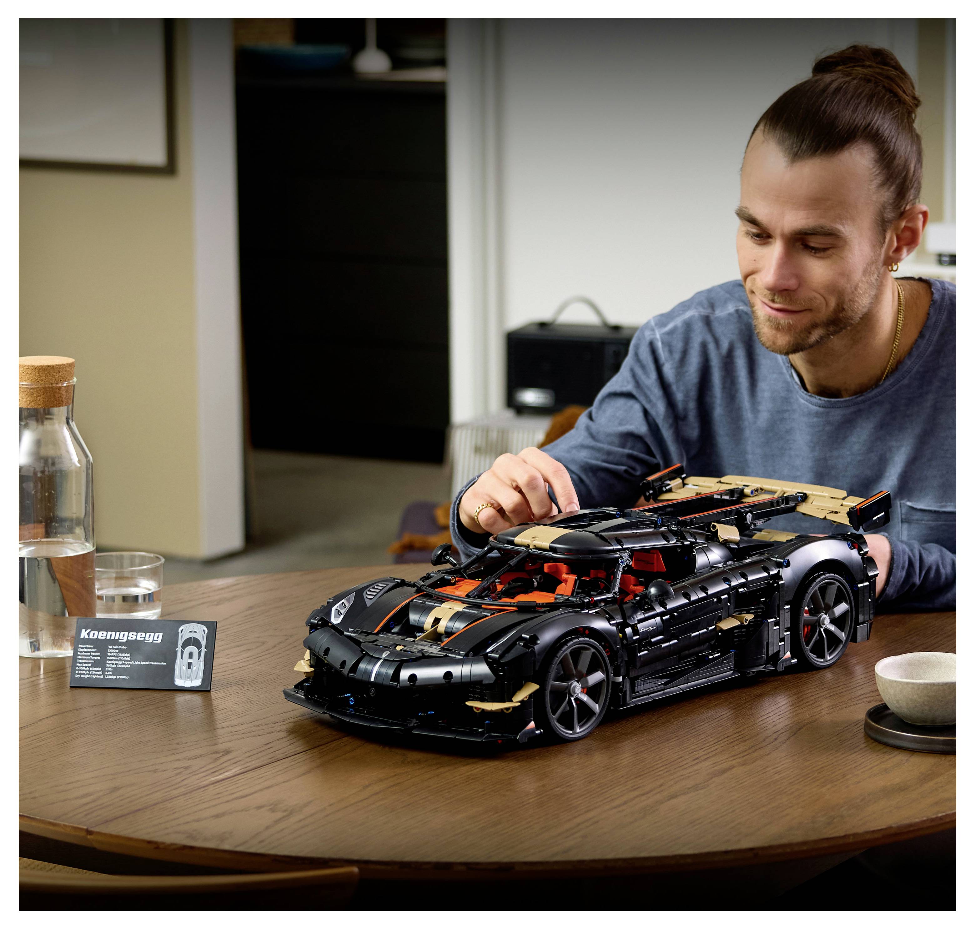 Muž skladá detailný čierny model automobilu LEGO Koenigsegg za stolom v interiéri.