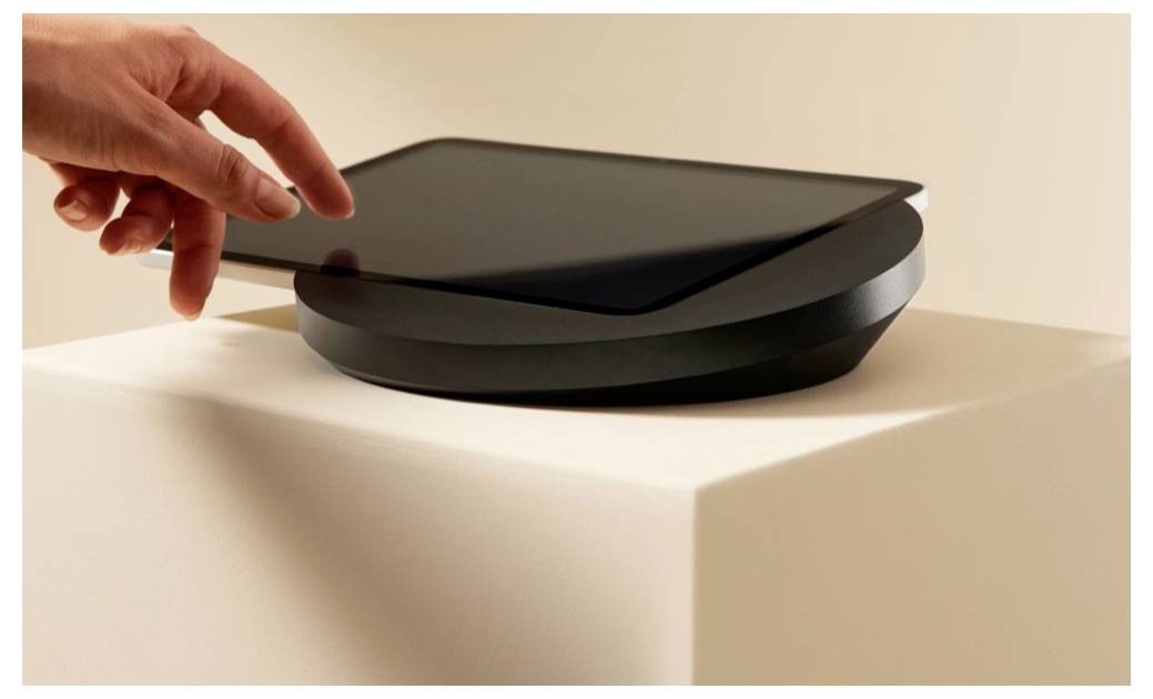 Ruka zdvíha veko elegantného čierneho elektronického zariadenia na bielom podstavci.