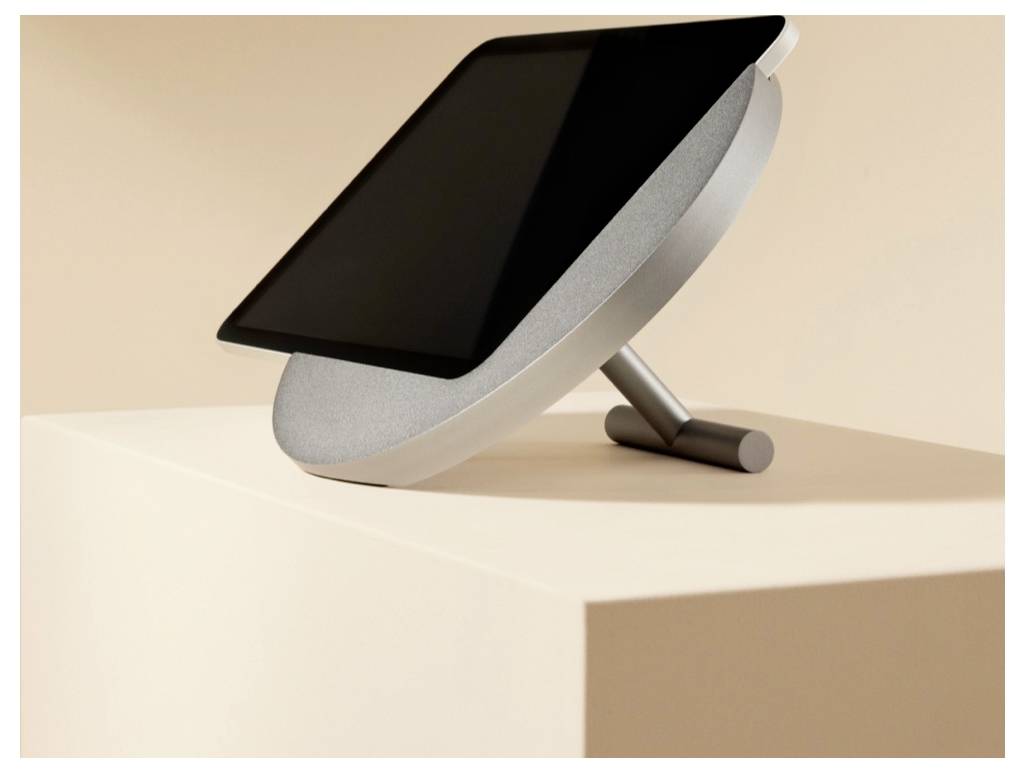 Čierny tablet alebo monitor na naklonenom striebornom statíve, umiestnený na béžovom podstavci v minimalistickom študiovom prostredí.