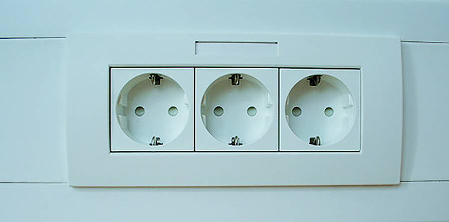 Tri európskych nástenných elektrických zásuviek v bielom paneli na svetlej stene.