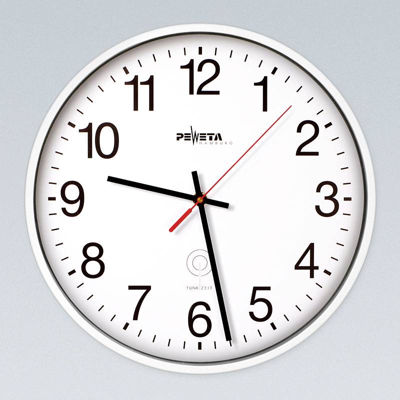 Zblízka biely analógový nástenný hodiny s čiernymi číslicami a ručičkami ukazujúcimi približne 9:29, plus červená sekundová ručička.