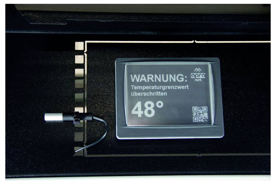 Elektronický displej s nemeckou výstrahou "WARNUNG: Temperaturgrenzwert überschritten" s teplotným odčítaním 48° a QR kódom, ktorý označuje výstrahu proti prehriatiu.