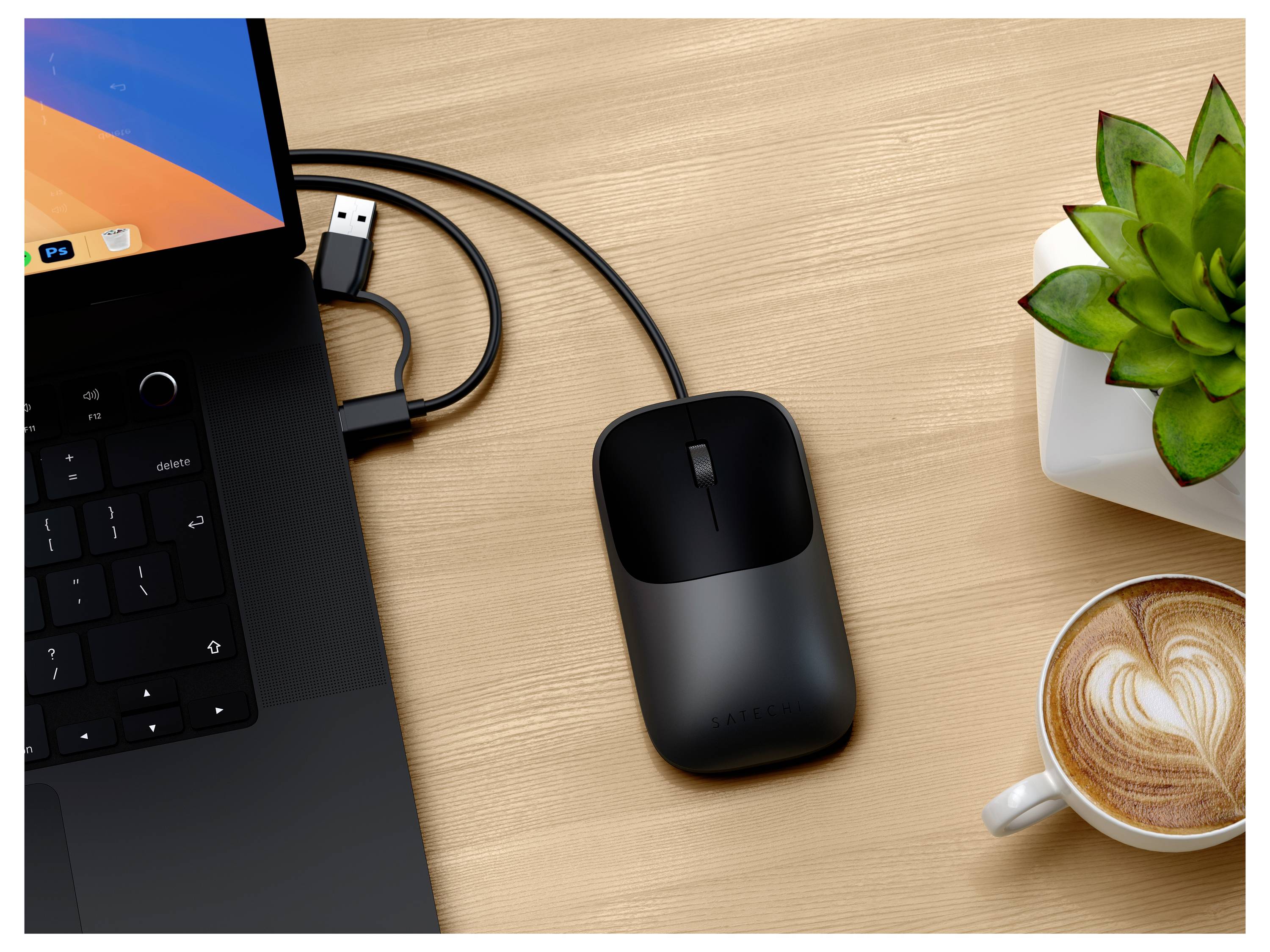 Pohľad zhora na notebook s USB myšou, nabíjacím kábľom, malou izbovou rastlinou v kvetináči a šálkou latte na drevenom stole.