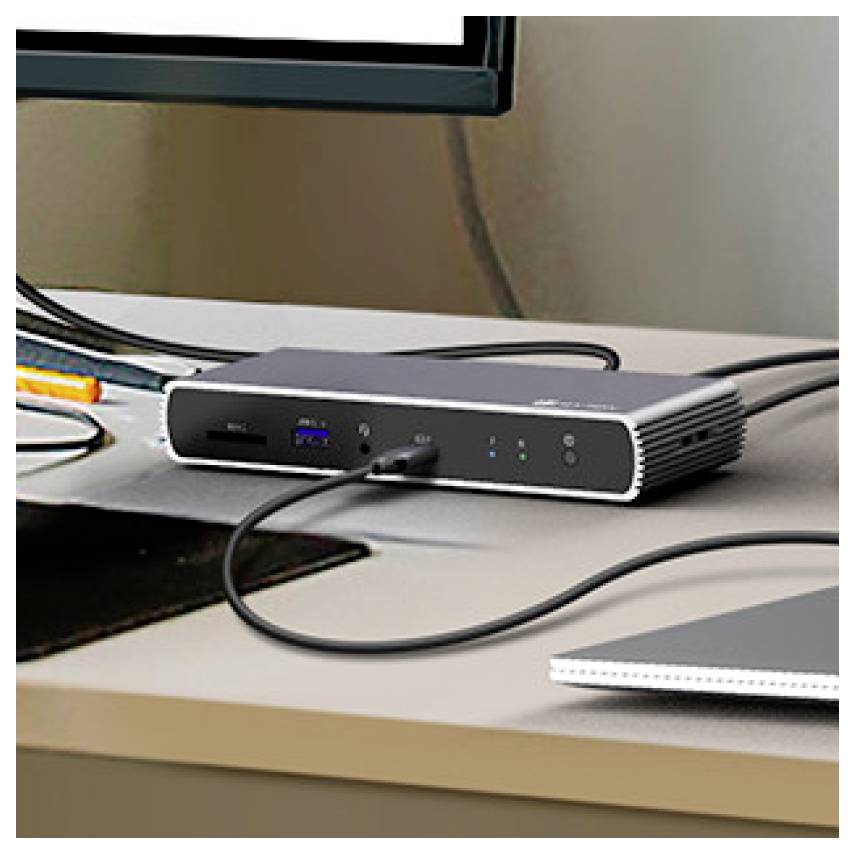 Malá čierna dokovacia stanica na stole s USB a ďalšími káblami zapojenými pod monitorom.