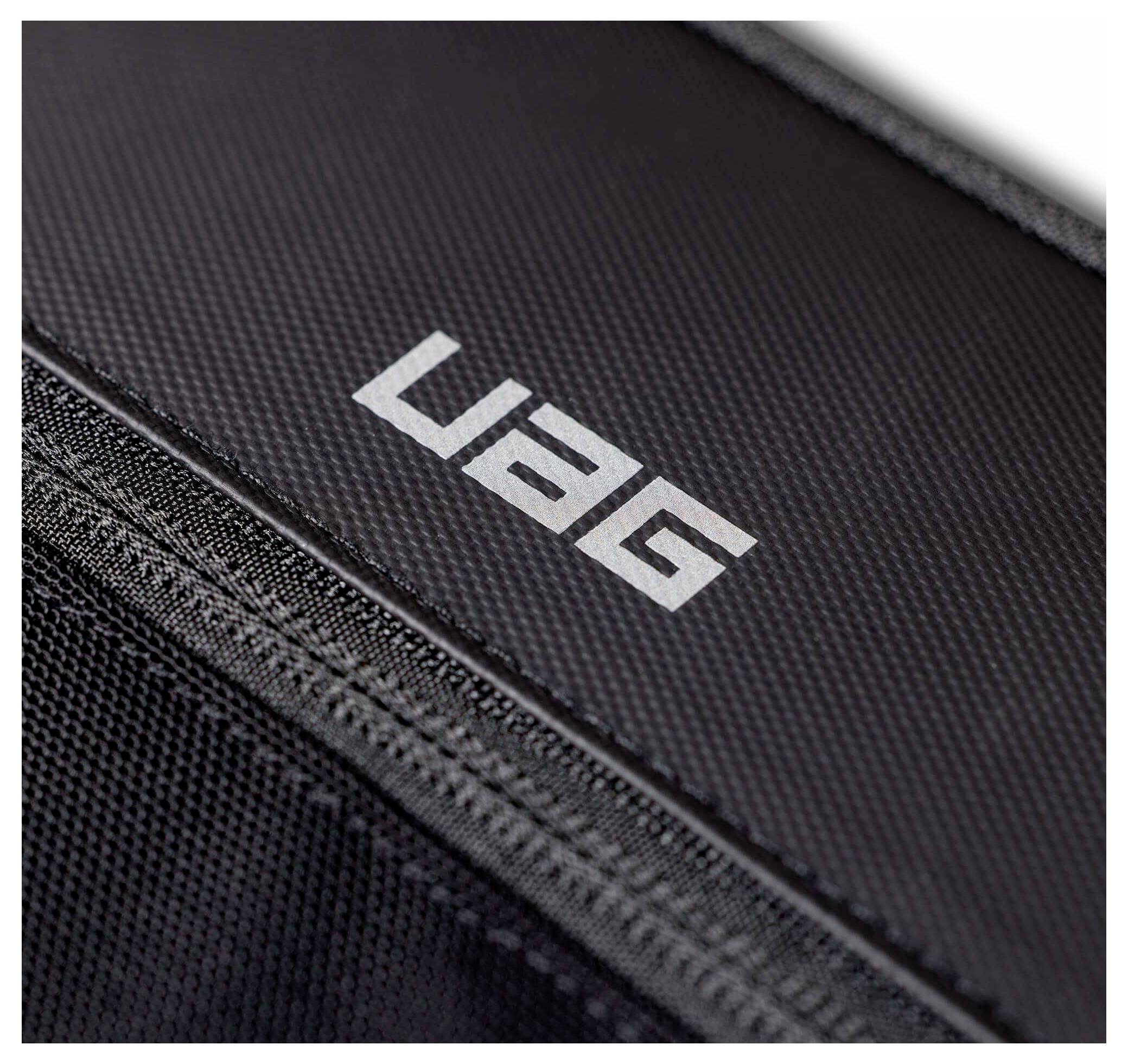 Zblízka čiernej textúrovanej tašky alebo puzdra s bielym logom „UAG" a viditeľným zipsom.