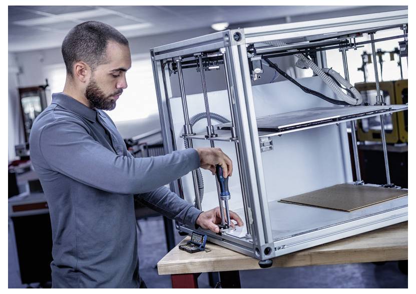 Technik upravuje 3D tlačiareň na pracovnom stole, utahovať nástroj v blízkosti rámu stroja v dielni.