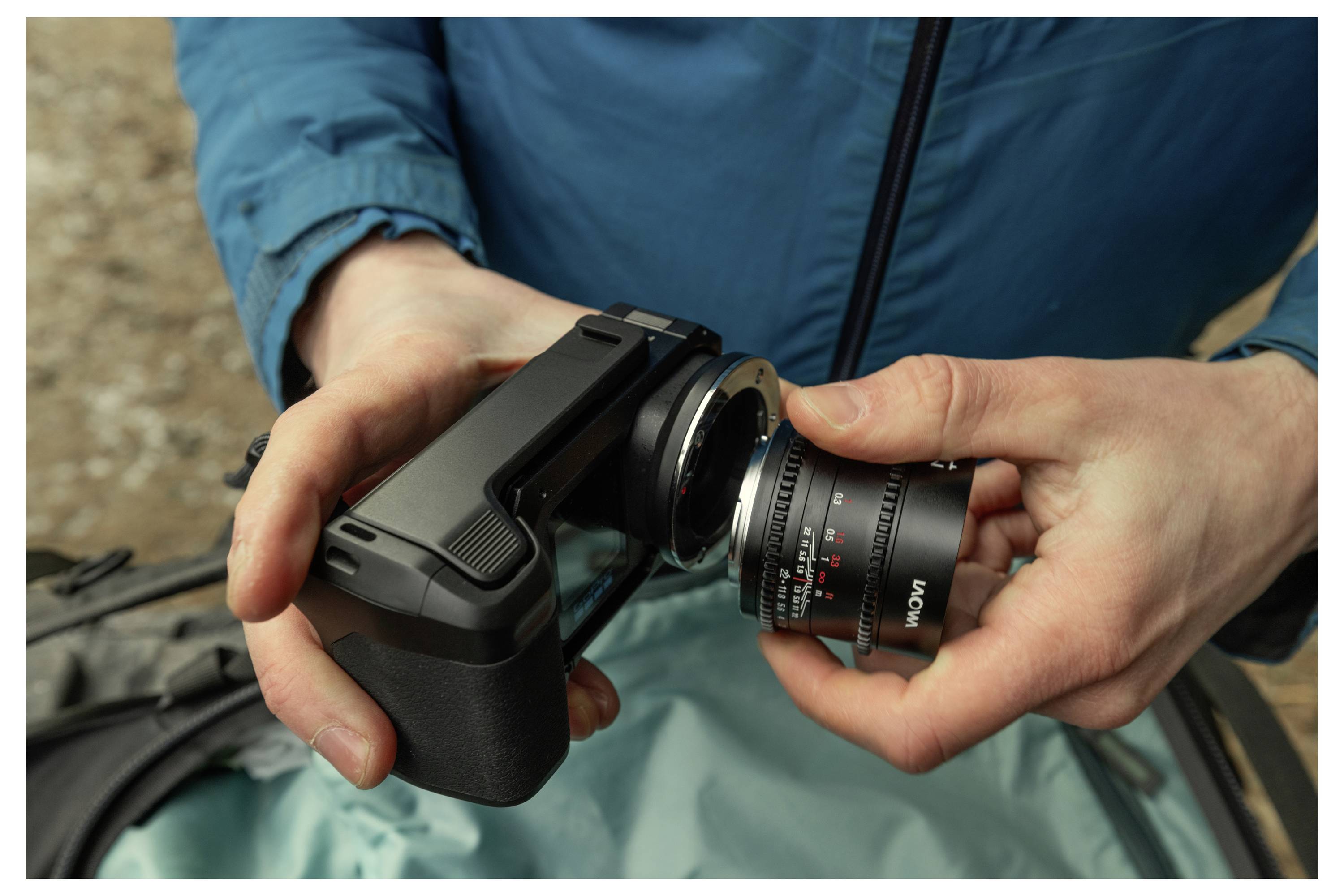 Zblízka zobrazenie osoby pripájajúcej objektív fotoaparátu na ručný fotoaparát na teal kabáte, pripravujúce fotoaparát na použitie.