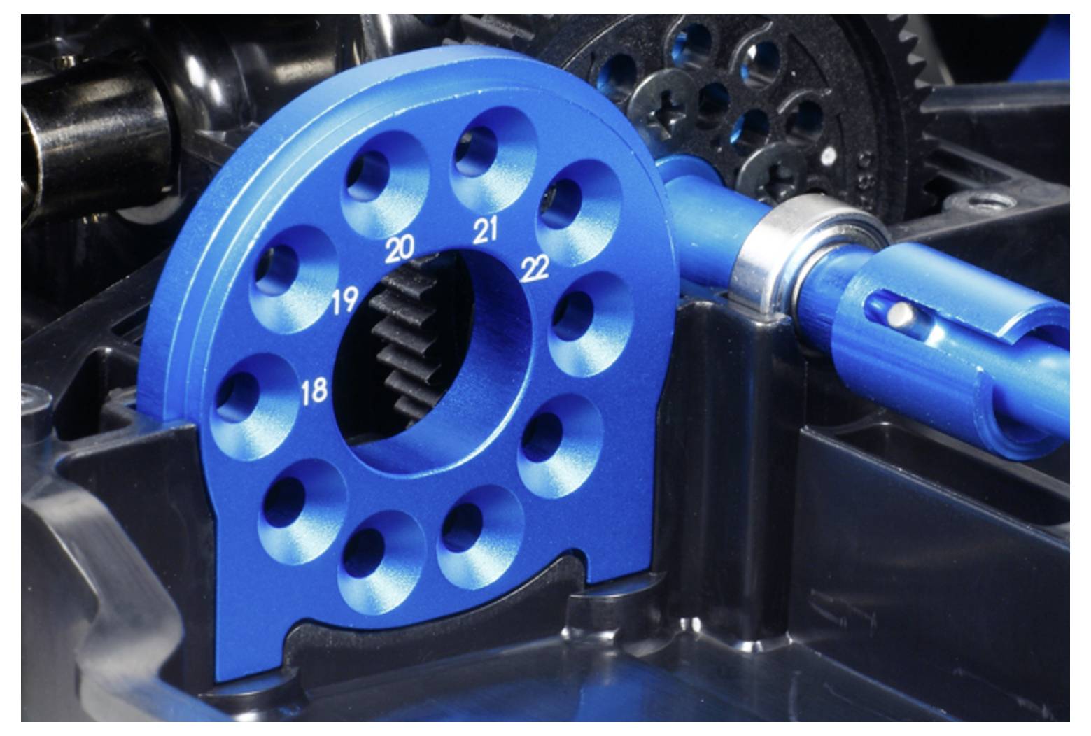 Zblízka modrého anodizovaného mechanického ozubeného kolesa alebo regulačného kolesa s číselnými otvormi, namontovaného v rámci montážneho celku stroja.