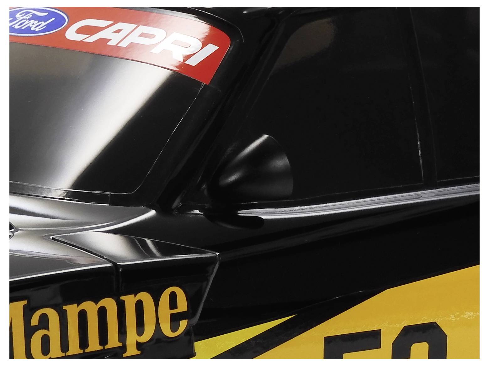 Zblízka čierne pretekárske auto Ford s nálepkami "CAPRI", ktoré zobrazuje predné sklo, bočné zrkadlo a žlté číselné grafiky.