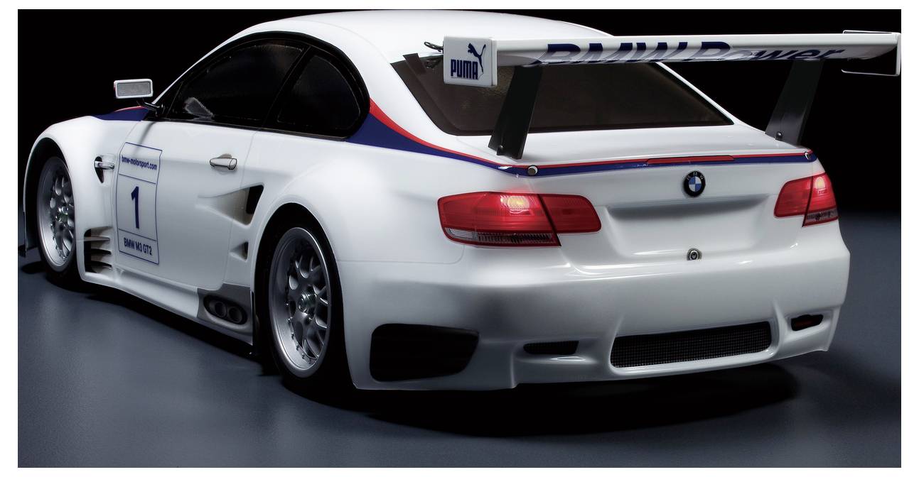 Zadný pohľad na biely pretekársky automobil BMW s číslom 1, veľkým zadným krídlom a značkou PUMA, zobrazený v študiovanom prostredí.