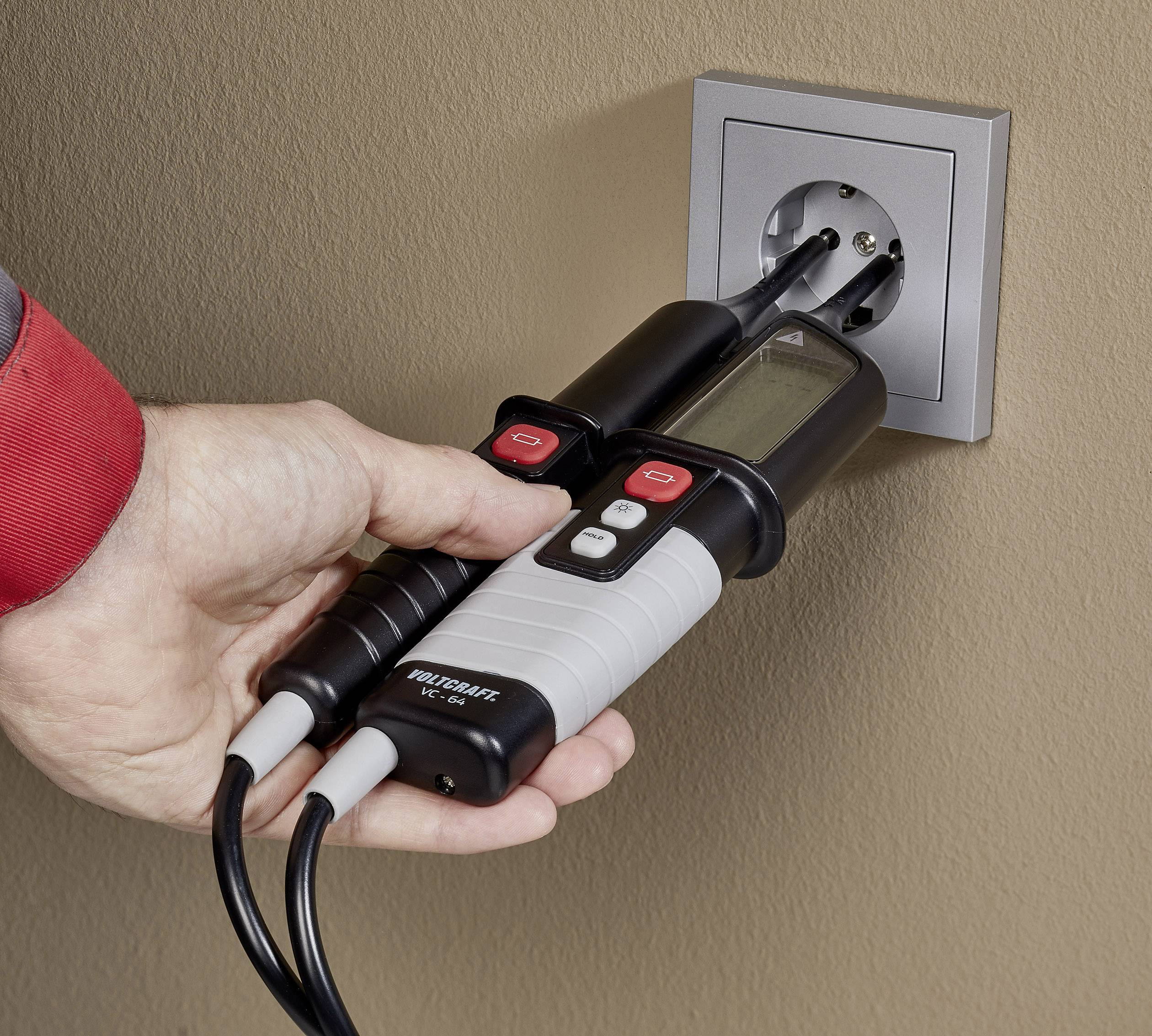 Jedna ruka drží elektrický tester pri elektrickej zásuvke, aby skontrolovala elektrické napätie.