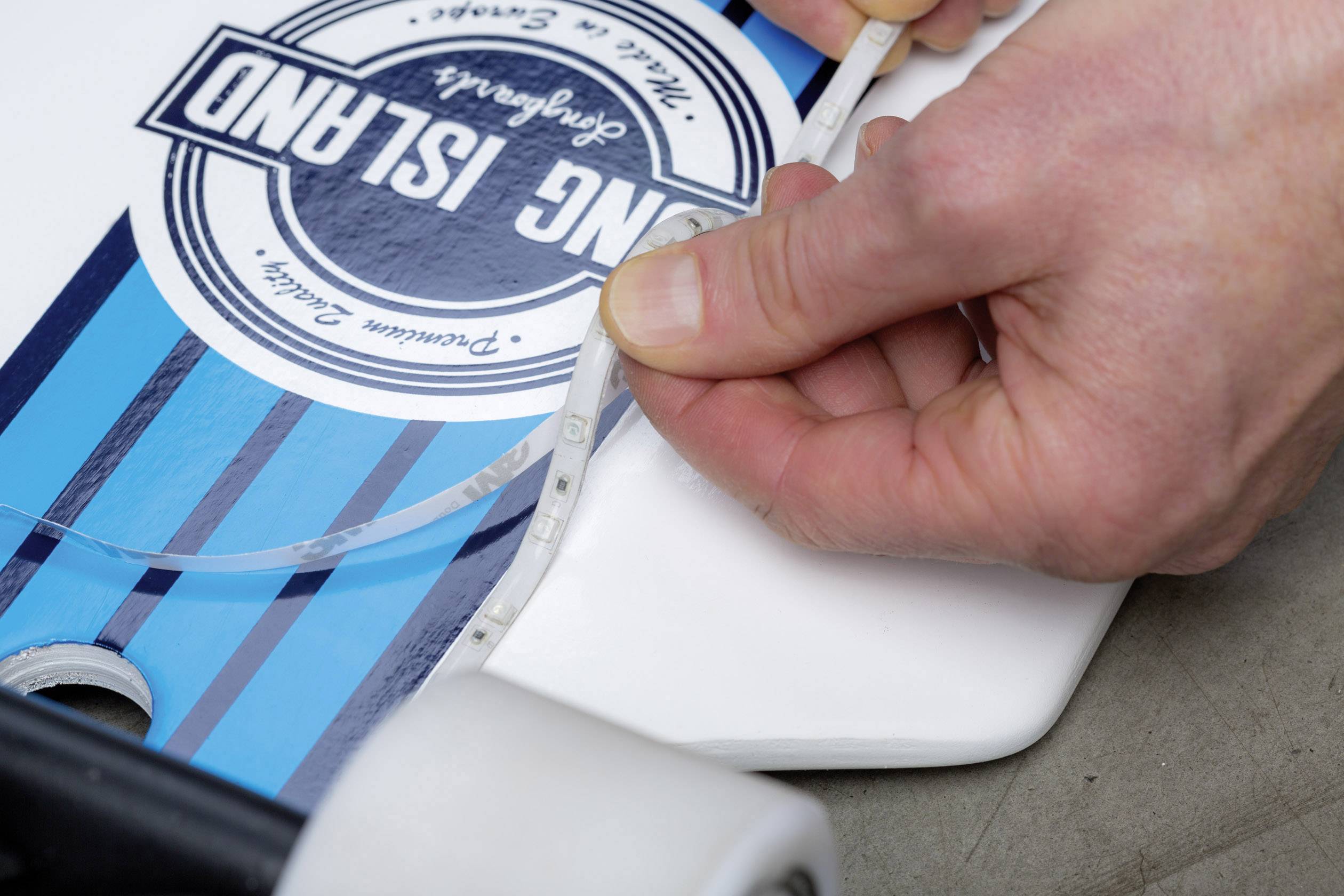 Osoba meria šírku skateboadu s nápisom 'Long Island' pomocou meracieho pásma.