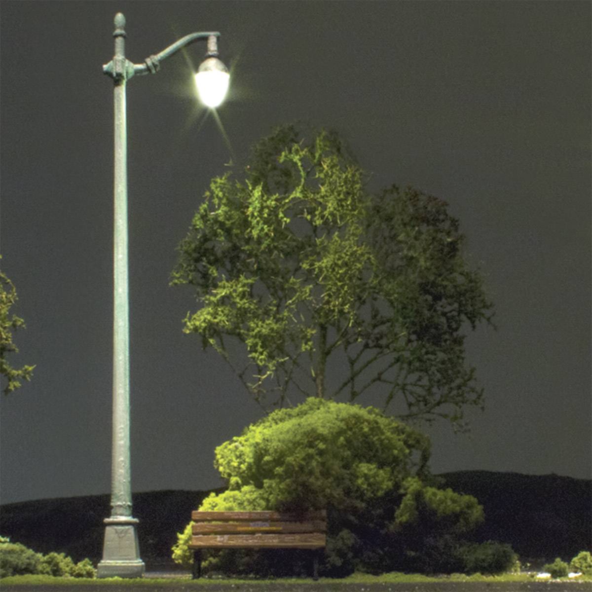 Pouličná lampa osvetľuje prázdny park s lavičkou a stromami v noci.