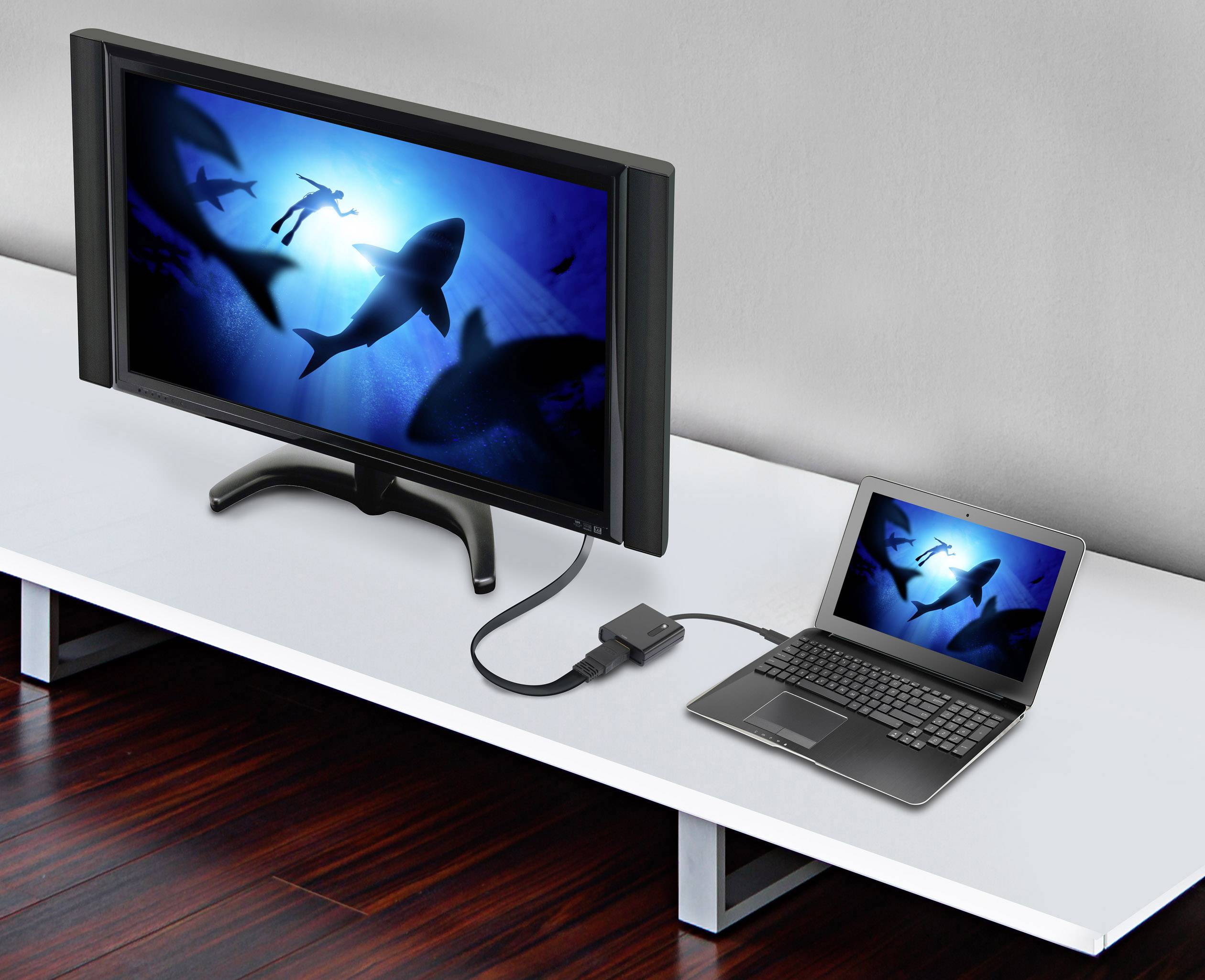 Laptop je prostredníctvom kábla prepojený s väčším monitorom. Na oboch obrazovkách je vidieť obrázok žralokov v oceáne.