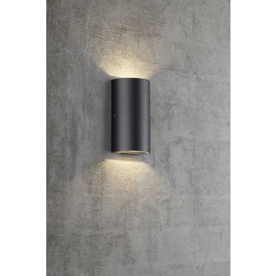 Nástenná lampa v modernom, valcovitom dizajne, ktorá smeruje svetlo nahor a nadol na sivej betónovej stene.