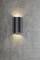 Nástenná lampa v modernom, valcovitom dizajne, ktorá smeruje svetlo nahor a nadol na sivej betónovej stene.