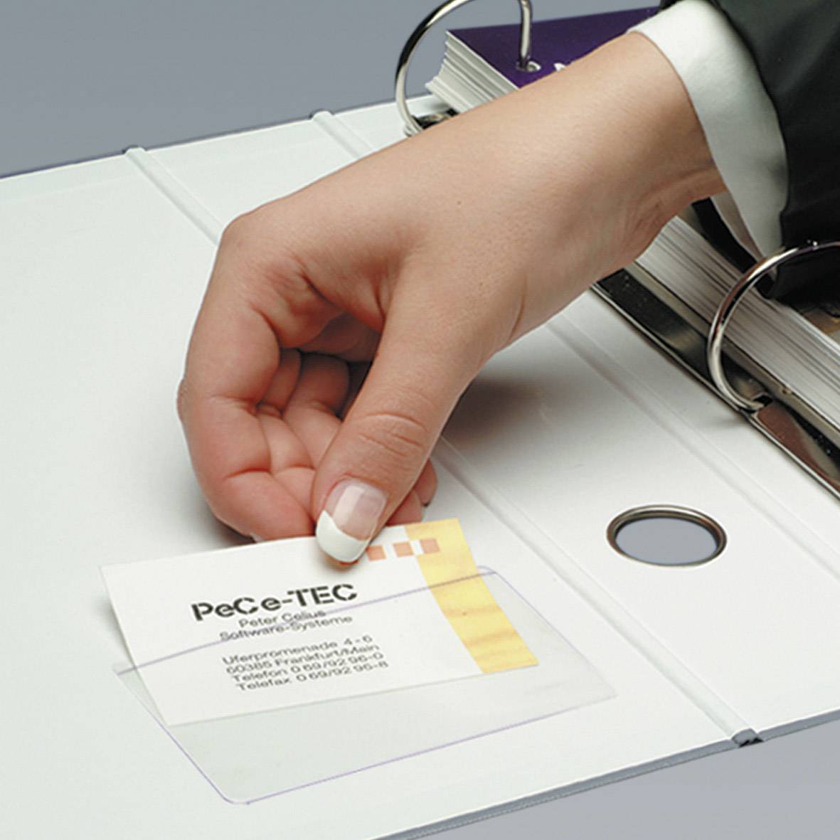 Ruka vkladá vizitku s nápisom 'PeCe-TEC Paper' do bieleho zakladača. Zakladač leží na stole.