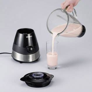 Osoba nalieava ružový smoothie z mixéra do skla. Vedľa toho stojí základňa mixéra na sivom povrchu.