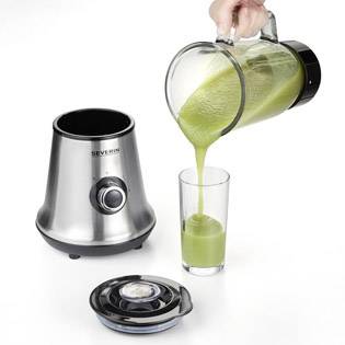 Ruka nalievajú zelené smoothie z mixéra do skla. Mixér stojí na stole s odňatým vekom.