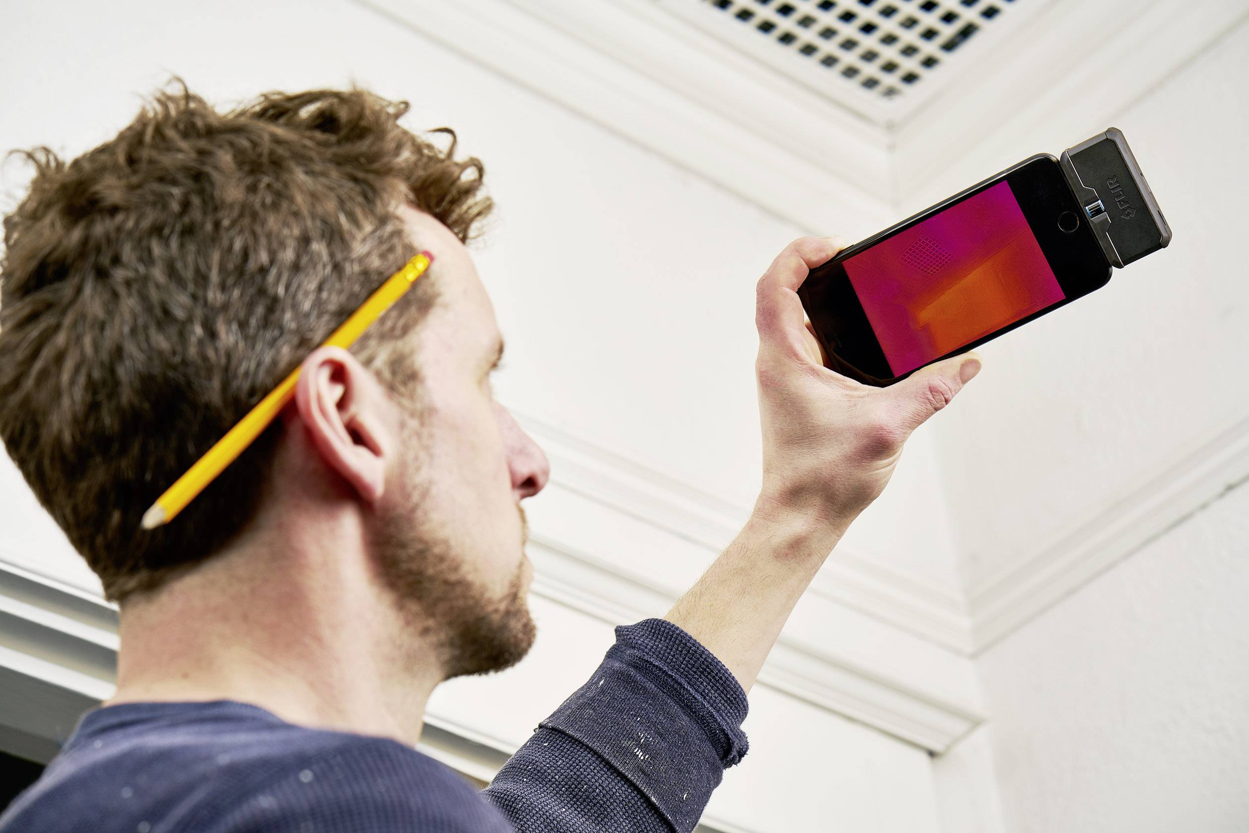 Muž drží smartfón s termokamerou vo vzduchu, aby zmerial teplotné rozdiely na strope.
