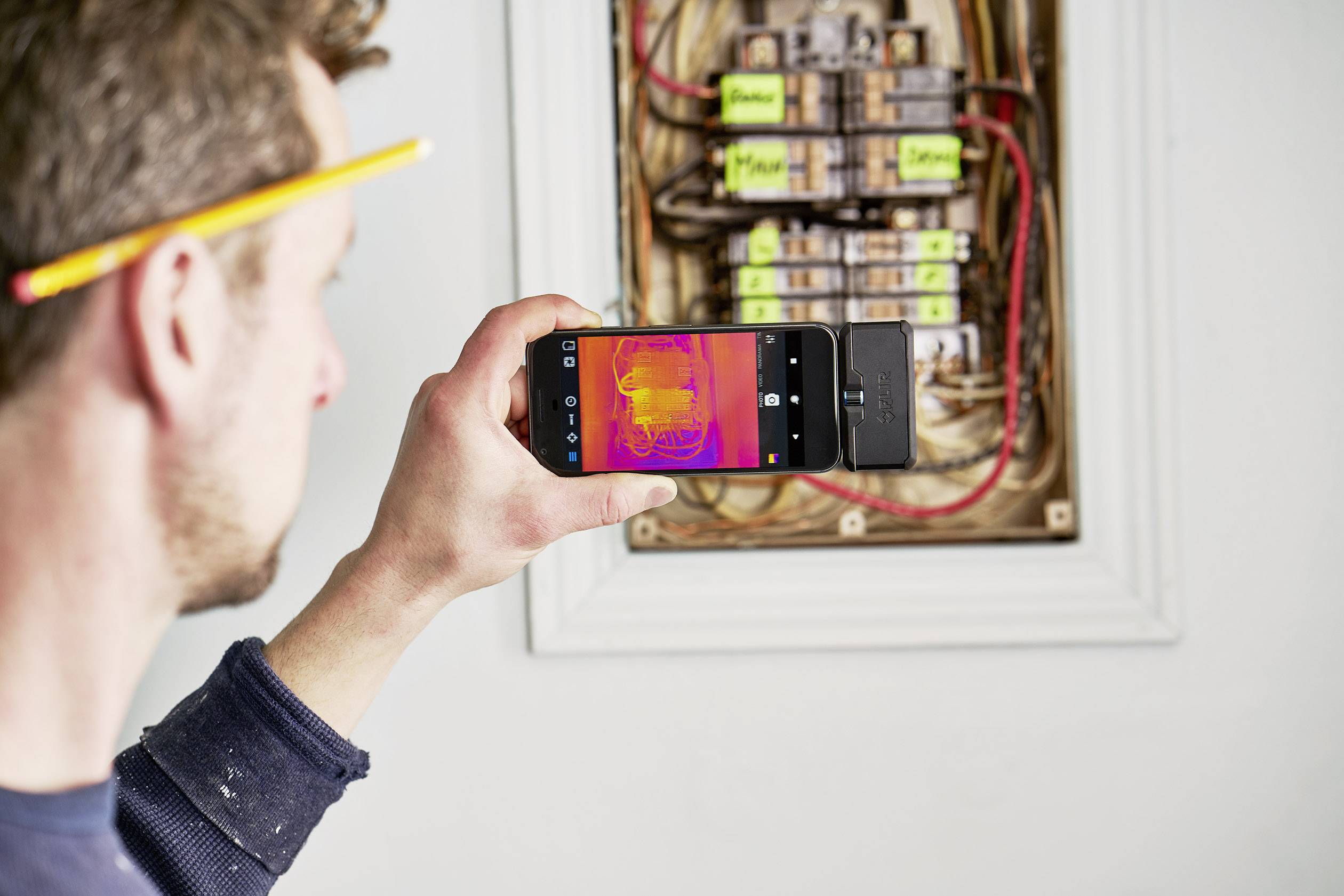 Muž fotografuje tepelné žiarenie otvorenej poistkovej skrine pomocou smartfónu.