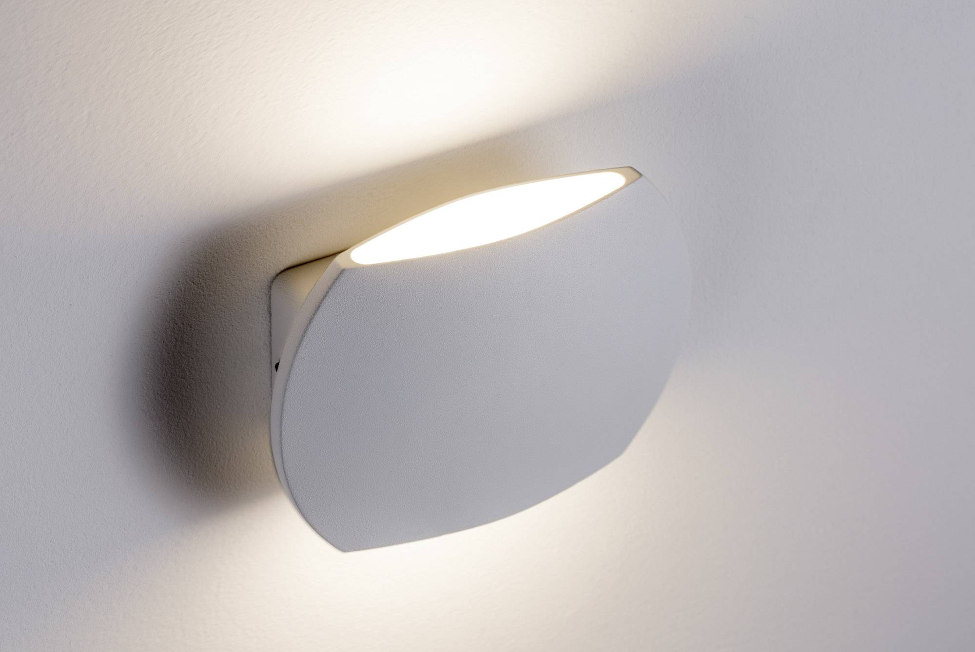 Moderná biela nástenná lampa na stene, ktorá vyžaruje teplé svetlo smerom nahor a nadol.