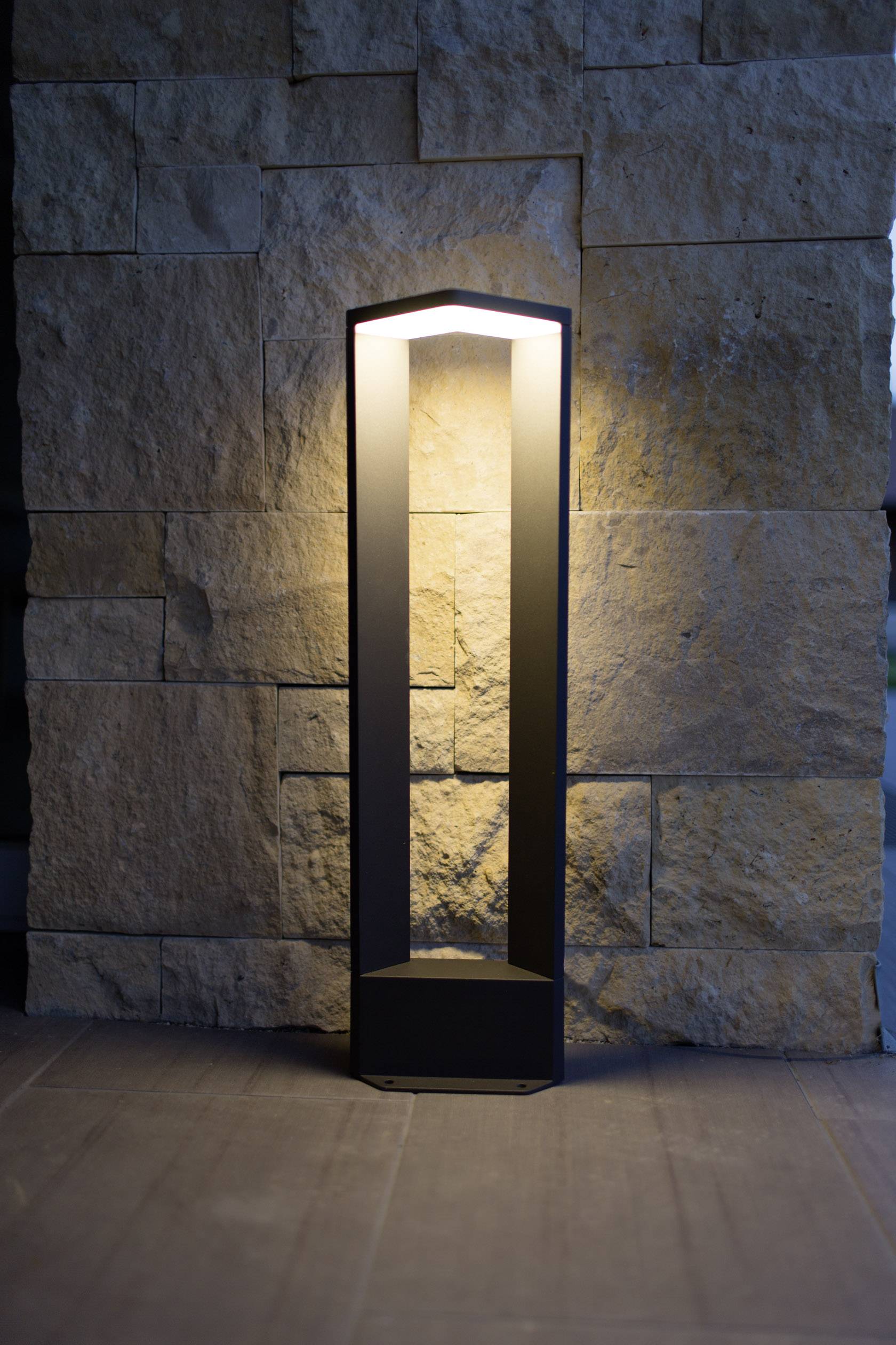 Moderná čierna stojanová lampa osvecuje stenu z hrubého prírodného kameňa a vytvára teplú a útulnú atmosféru.