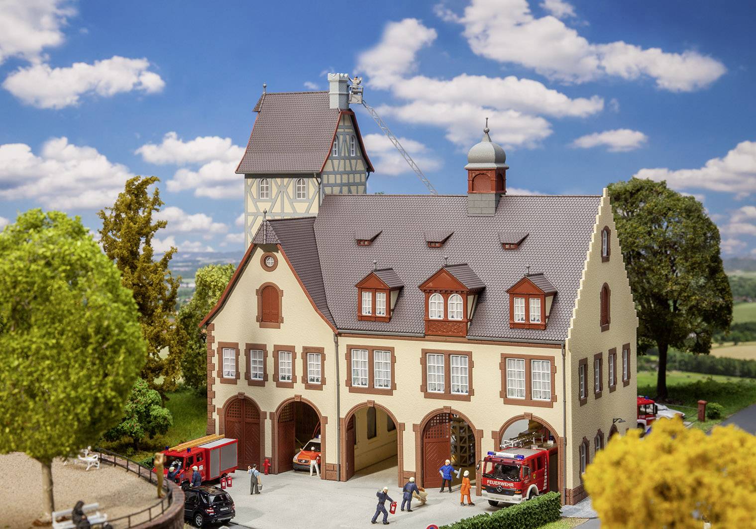 Miniaturový model hasičskej stanice s červenými bránami, s detailmi ako ľudské figúrky a hasičské vozidlá pred budovou.