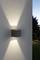 Vonkajšia nástenná lampa svieti nahor a nadol, vytvára štýlový svetelný vzor na betónovej stene za súmraku.