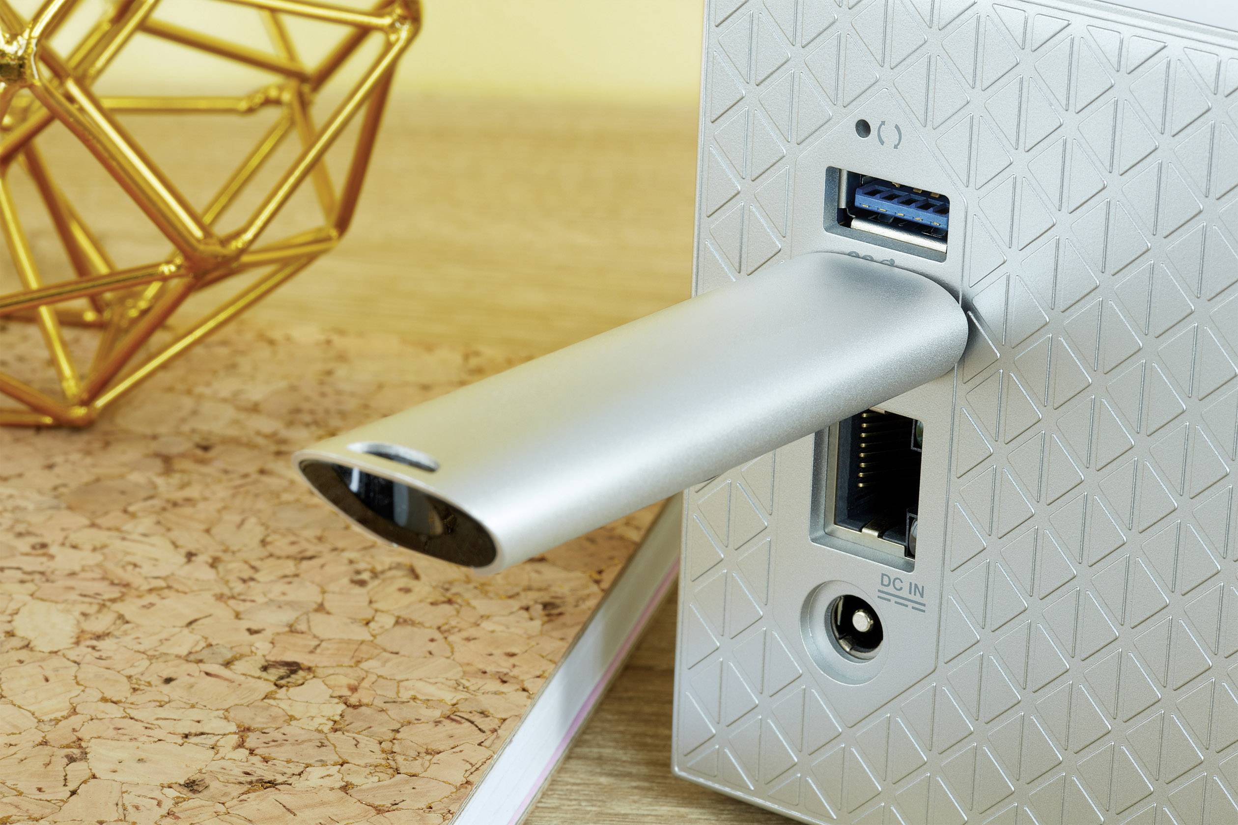 Strieborný USB kľúč je zasunutý do moderného zariadenia so geometrickým vzorom na zadnej strane. Vedľa neho sú viditeľné ďalšie konektory.