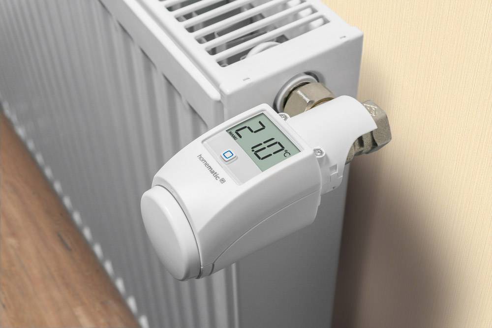 Digitálny termostatický ventil na radiátore ukazuje '21,0°C'. Je namontovaný na krémovej stene.