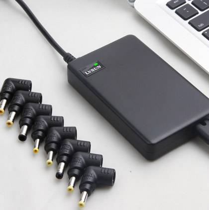 Nabíjačka laptopa s odnímateľnými adaptérmi s rôznymi veľkosťami konektorov leží vedľa klávesnice laptopa.