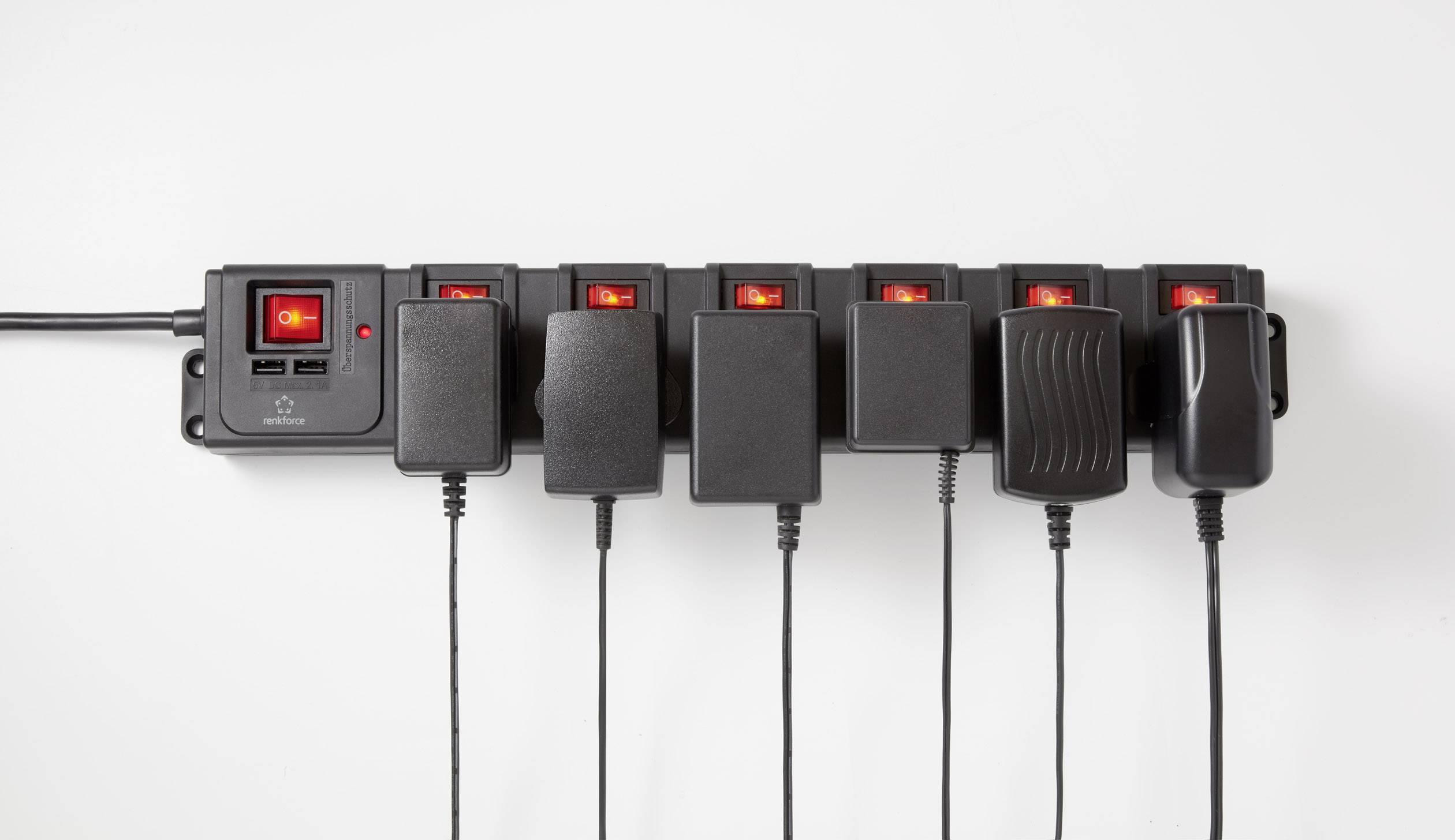Elektrická predlžovacia lišta so siedmimi zapojenými sieťovými adaptérmi a červenými spínačmi. Všetky zariadenia sú zapojené a zapnuté.
