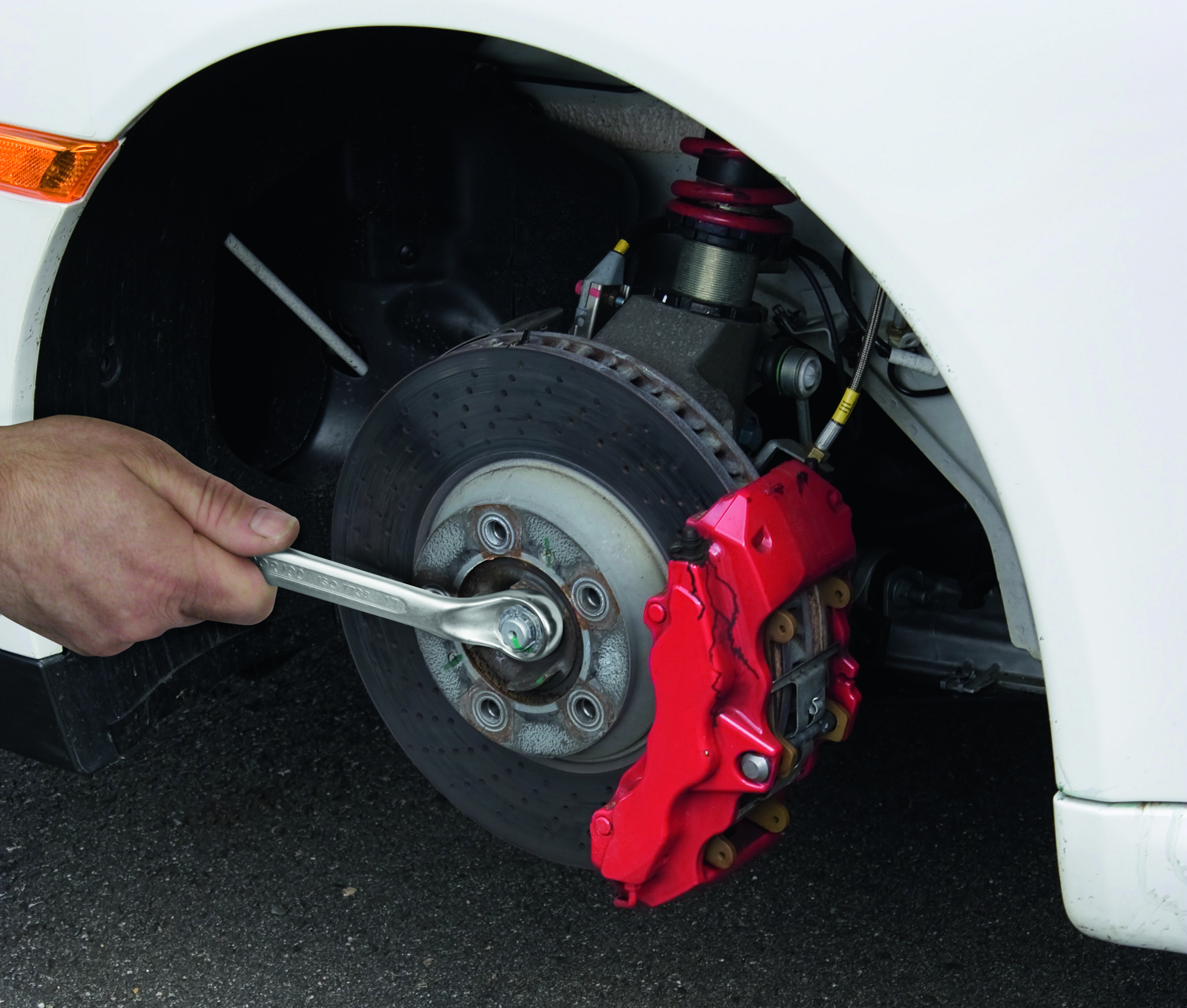 Ruka dotiahuje maticu kolesa na bielom aute pomocou kľúča.