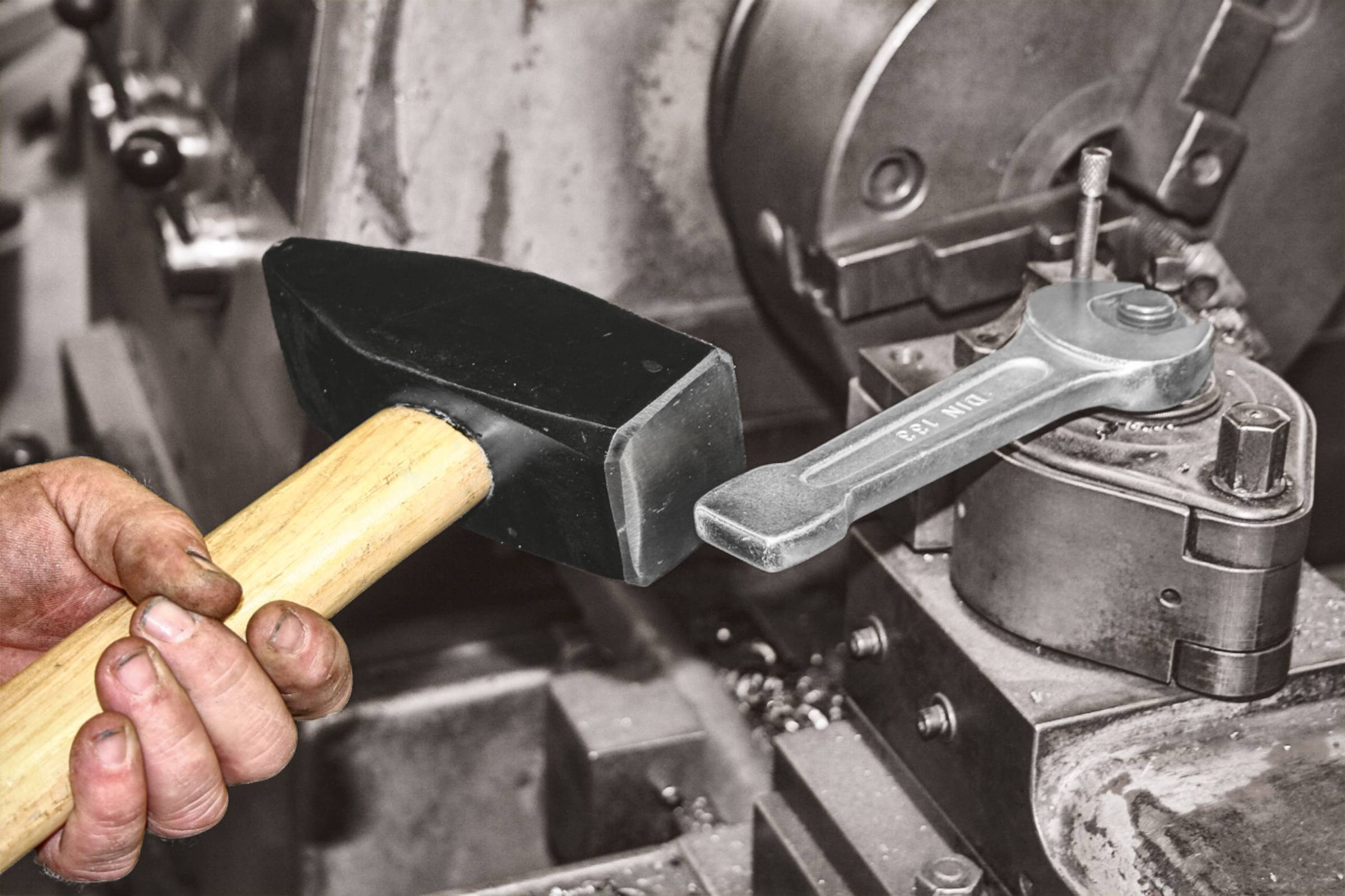 Osoba drží kladivo vedľa ťažkého priemyselného stroja. Dôraz je kladený na ovládanie strojového riadenia.