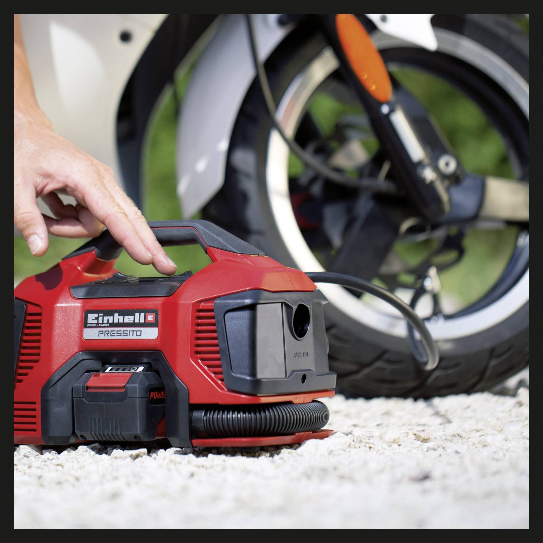 Osoba používa prenosný kompresor na nafúknutie pneumatiky motocykla. Kompresor je červený a praktický.