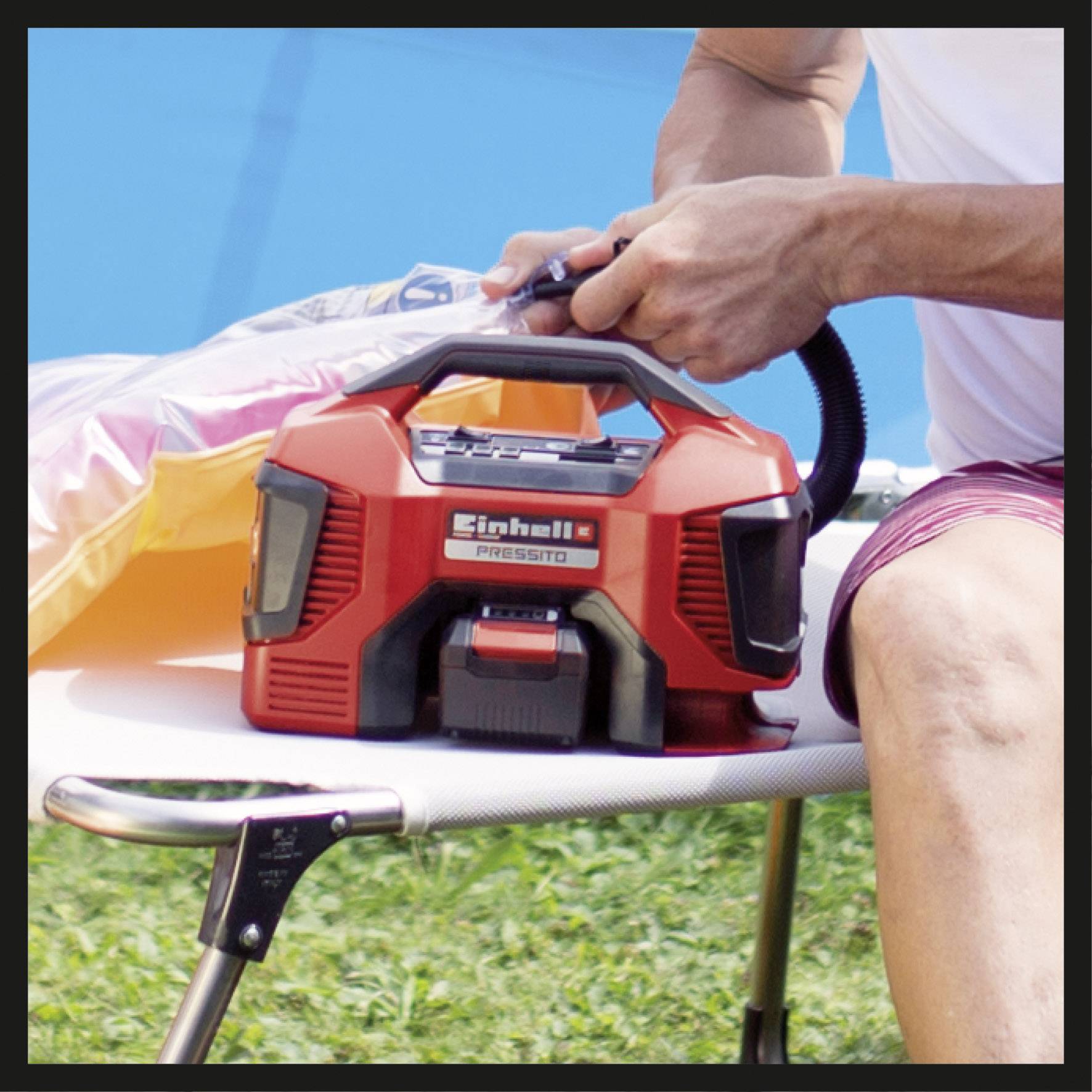 Osoba používa červenú elektrickú vzduchový pumpu na ležadle vonku, aby naplnila nafukovací predmet.