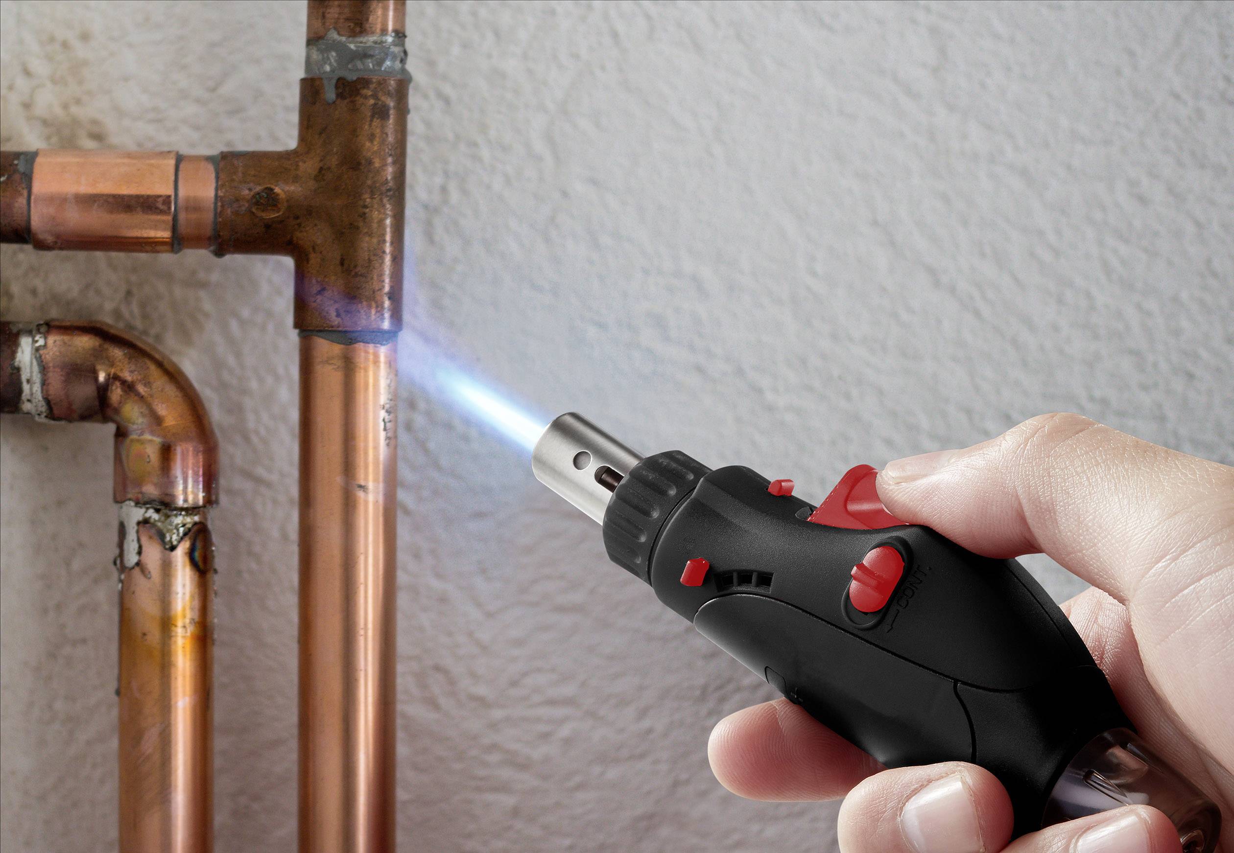 Jedna ruka drží malý horák a zohrieva medenú trubku, aby ju spájkovala.