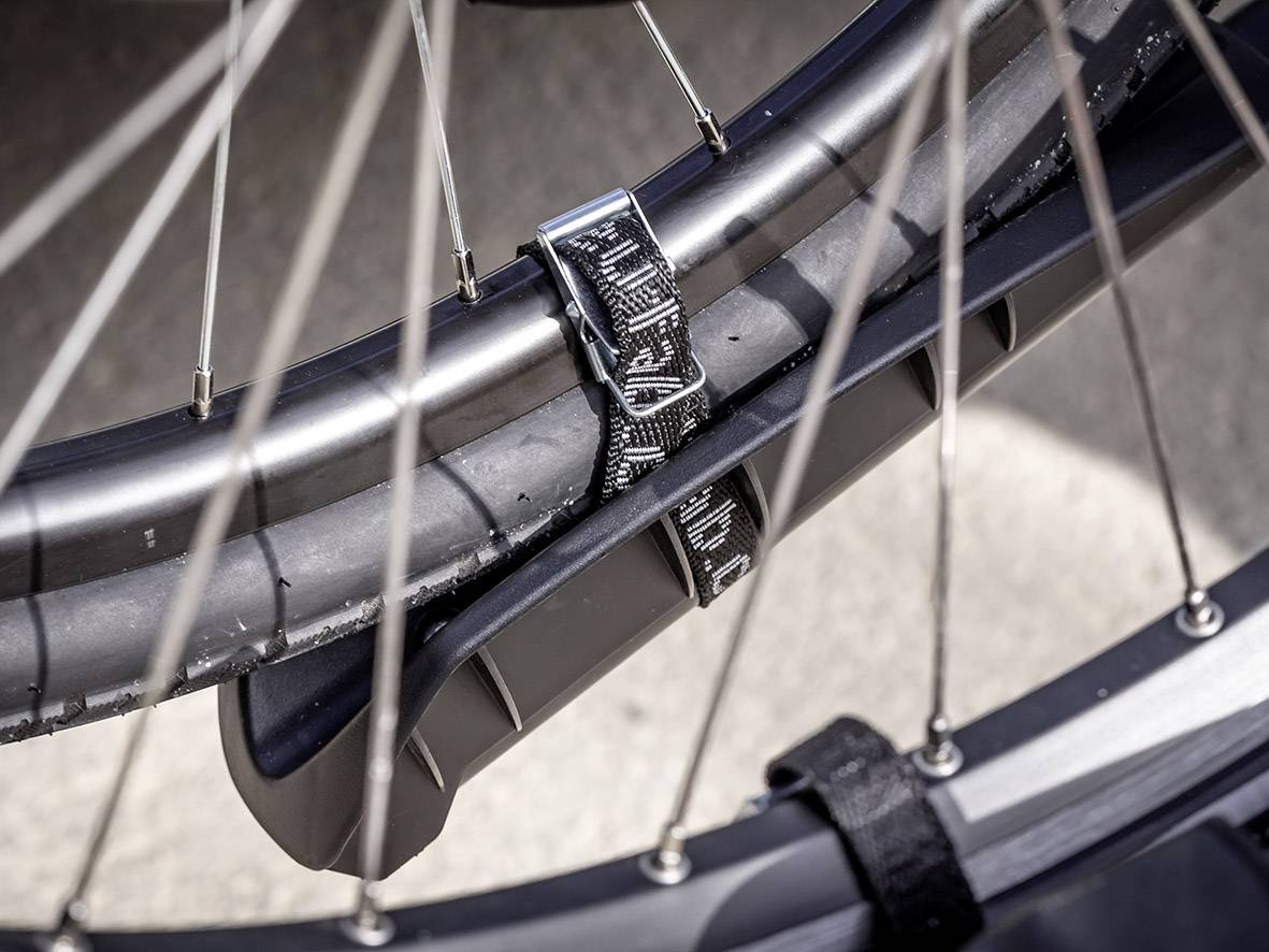 Detailný záber pneumatiky bicykla upevnenej na stojane čiernym popruhom. Sú viditeľné špice kolesa.