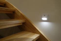 Drevené schodisko s osvetleným nástenným svietidlom. Svetlo osvecuje schody, aby umožnilo bezpečný výstup. Farba steny je svetlá.