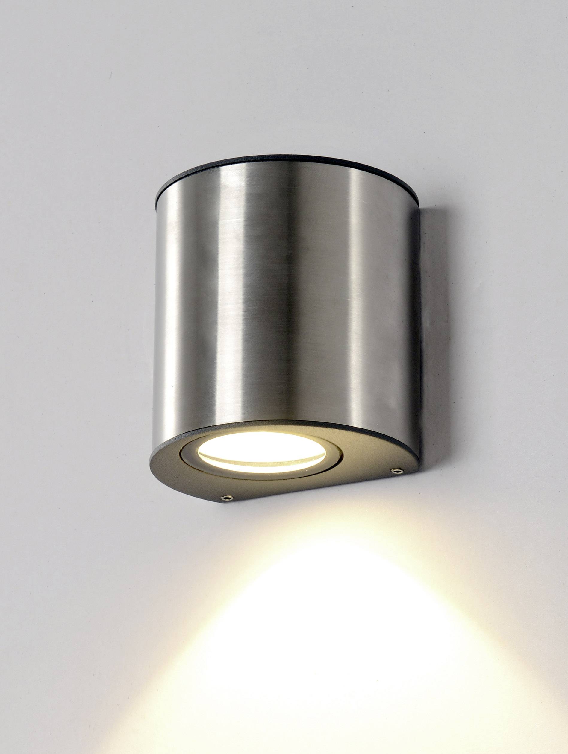 Valcovitá strieborná nástenná lampa vyžaruje svetlo smerujúce nadol.