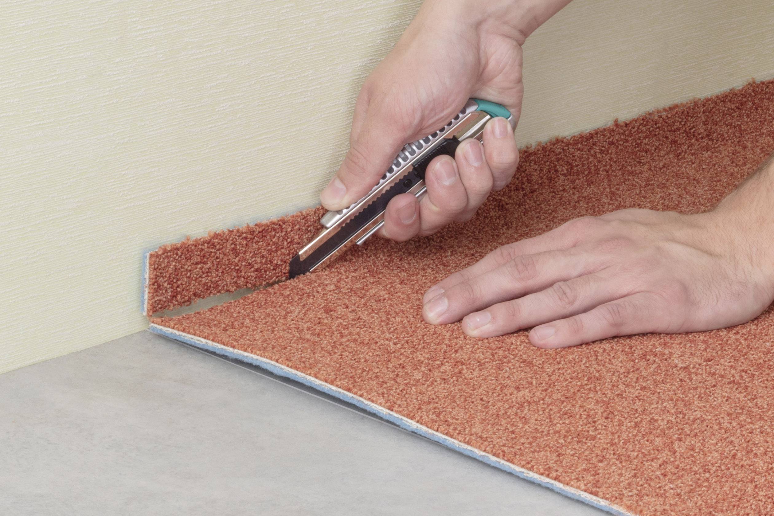 Osoba strihá červený koberec pomocou kobercového noža pozdĺž okraja, aby ho prispôsobila. Ruky sú viditeľné.
