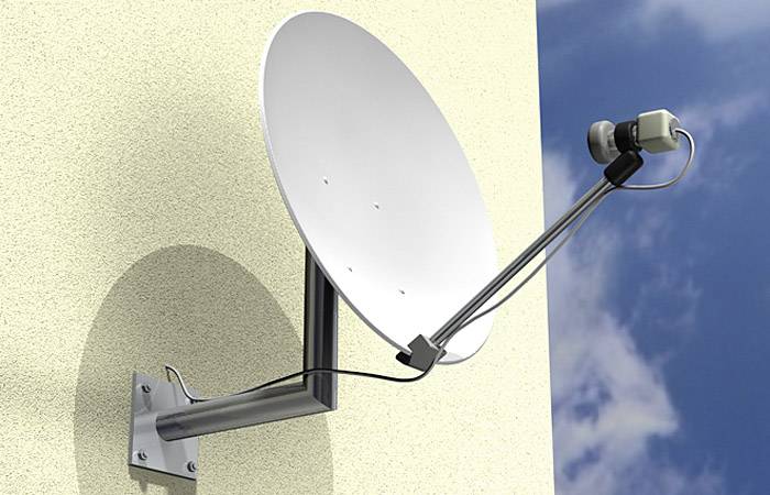 Satelitná parabola namontovaná na stene domu, smeruje k oblohe. Prijíma televízne signály z vesmíru. Vľavo je obloha mierne zahalená oblakmi.