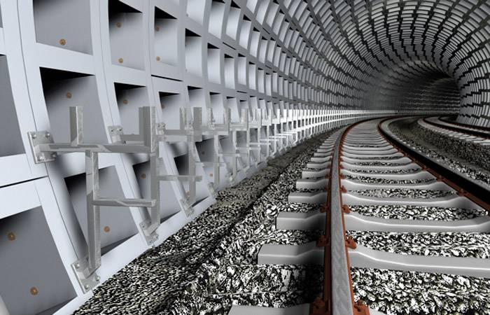 Tunel s koľajnicami a vystužnými betónovými stenami, ktoré sa tiahnu do diaľky. Kovové rámy sú pripevnené na stenách.