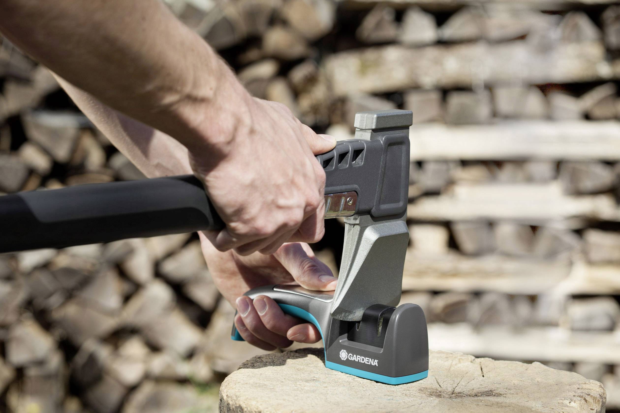 Dve ruky držia sekeru s kovovým chráničom na pni; v pozadí sú viditeľné naštosované polená.