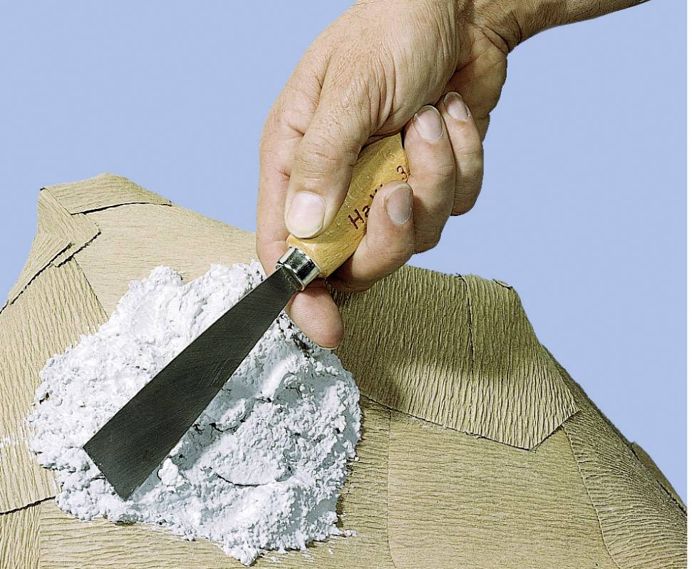 Jedna ruka drží murársku špachtľu a nanáša biely gips na štruktúrovaný povrch.