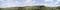 Panoramatický pohľad na zelenú kopcovitú krajinu pod modrým nebom s bielymi oblakmi.