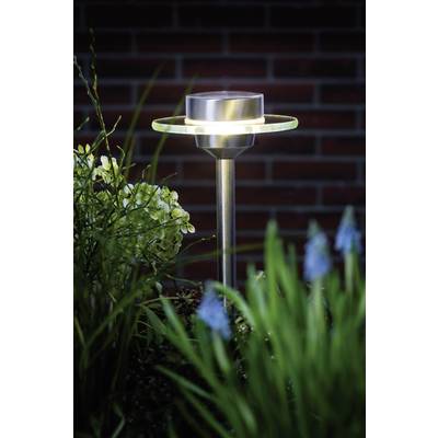 Solárna lampa v záhrade v noci, obklopená rastlinami, s tehlovou kulisou v pozadí.